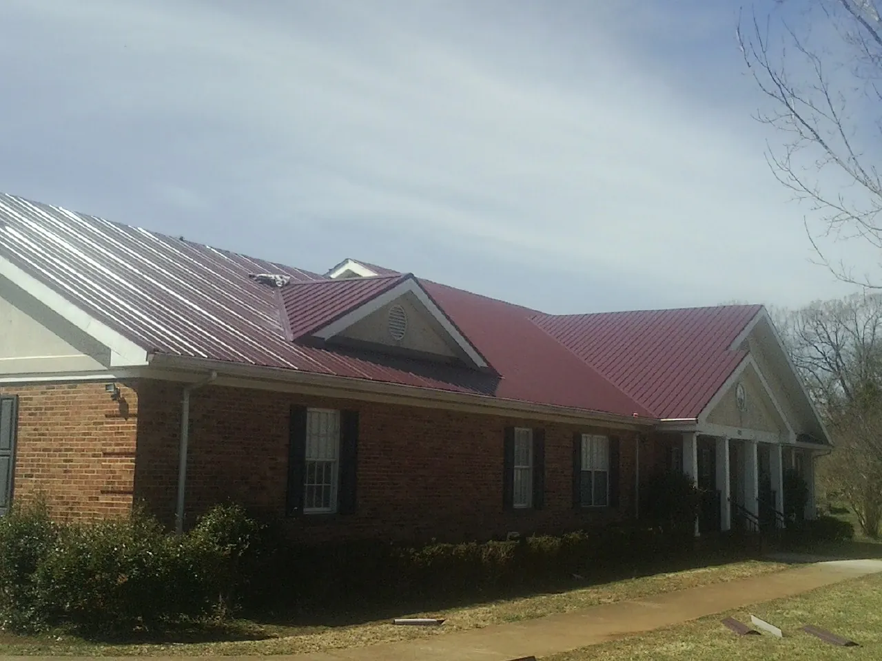Red metal roof with gabled entries on a long brick building, from a Hail Damage Roof Repair job in La Jolla