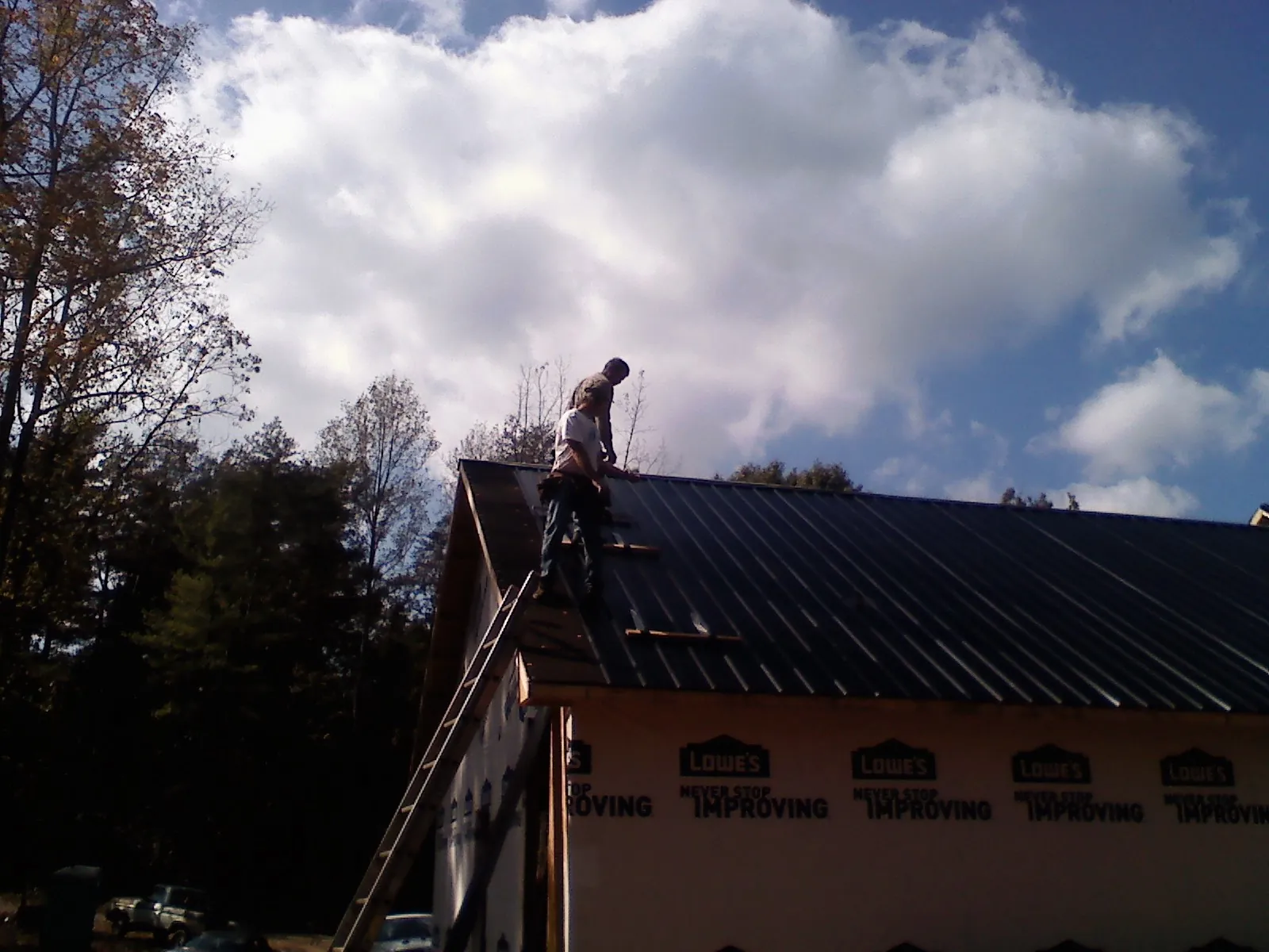 Roofer fastening dark metal panels high against a cloudy sky, from a Roof Inspection job in La Jolla